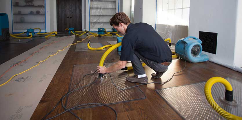 A man kneeling down on the floor with a hose attached to his head.